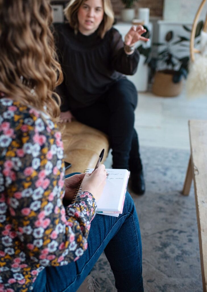 Two people discuss b2b content marketing in a comfortable and stylish modern office space, gesturing with their hands and taking notes in a spiral notebook.