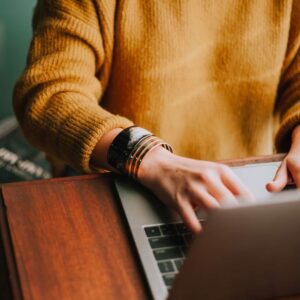 Woman in orange sweater typing on a laptop